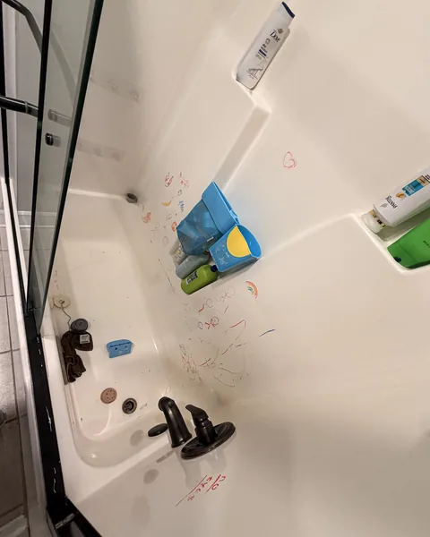 Bathtub and shower walls with marks and clutter before cleaning in a Lexington SC home